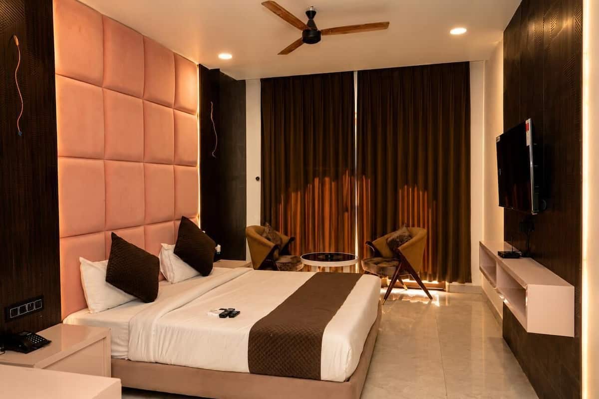 A modern hotel room with a large bed, a ceiling fan, a TV, a small table, and two chairs.