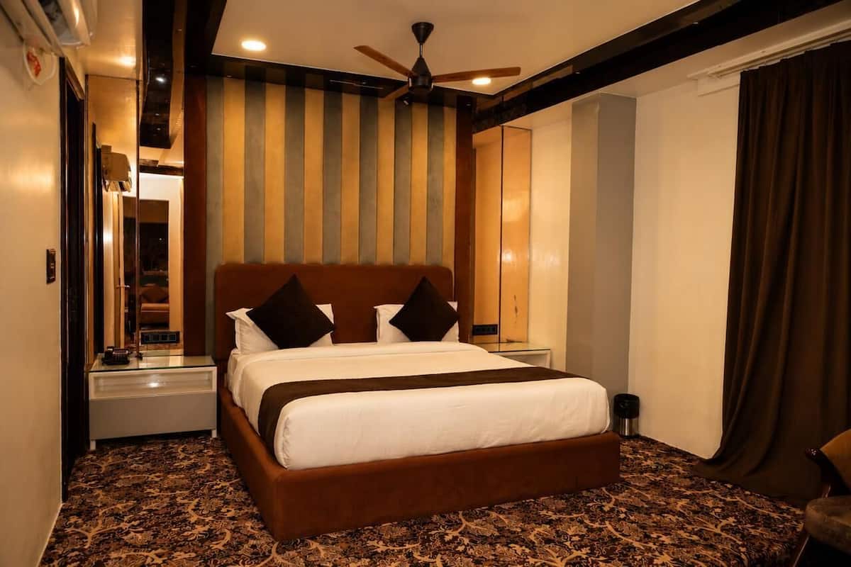 A hotel room with a large bed, a ceiling fan, a nightstand, a mirror, and a patterned carpet.