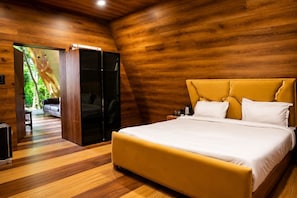 A bedroom with a wooden floor, a bed with a yellow headboard, a sofa, and a sliding door leading to a balcony. - Shiv Resort & Palace  (Shivpuri)