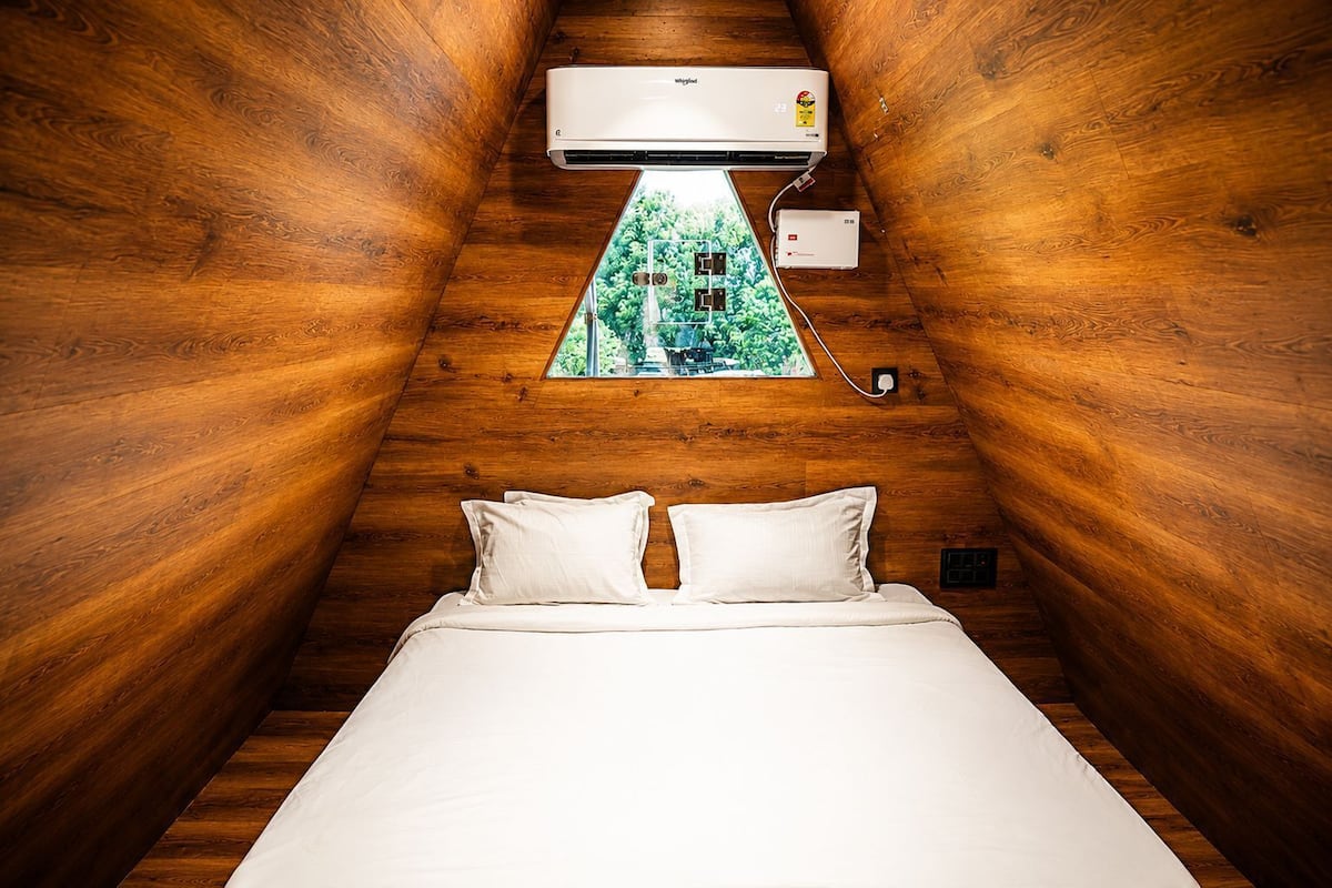 A room with a bed, wooden walls, a window with a view, and an air conditioning unit.