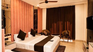 A modern hotel room with a bed, two chairs, a TV, and a ceiling fan.