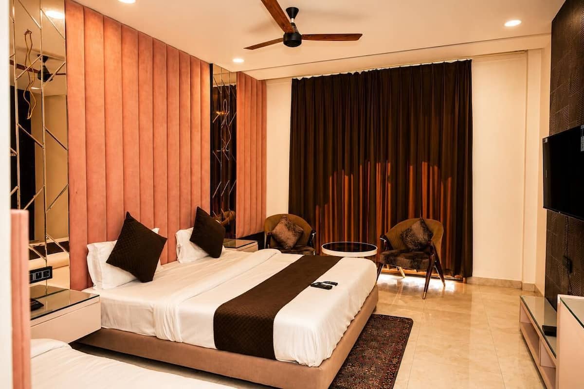 A modern hotel room with a bed, two chairs, a TV, and a ceiling fan.