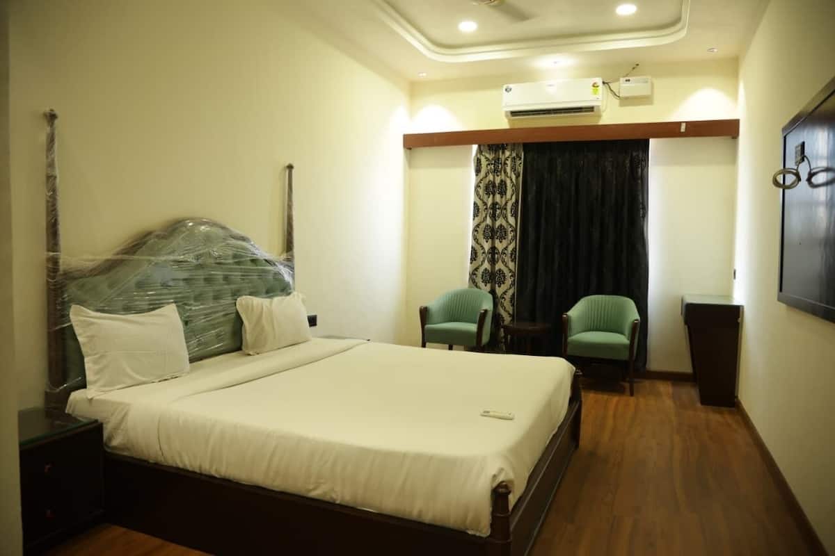 A neatly made bed with a headboard, a bedside table, a chair, and a small table with a lamp.
