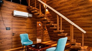 A wooden interior with a staircase, two chairs, a table, and an air conditioning unit.