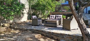 A stone patio with wicker furniture, including a sofa and two armchairs, surrounded by trees and a stone wall. - Authentic Sardinian villa in nature within walking distance of a beautiful beach (Siniscola)