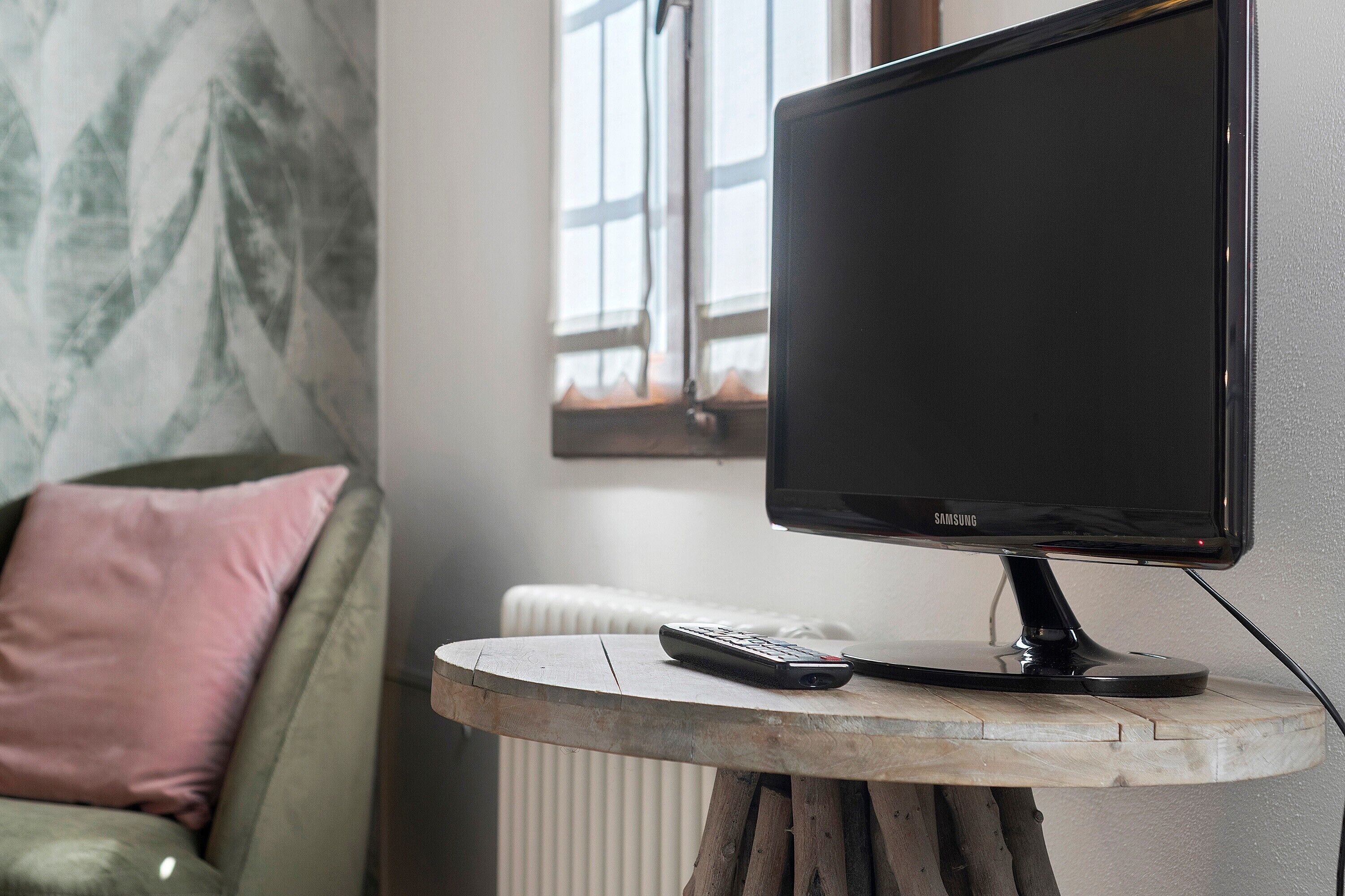 Un monitor nero Samsung su un piccolo tavolo di legno, con un telecomando appoggiato accanto.