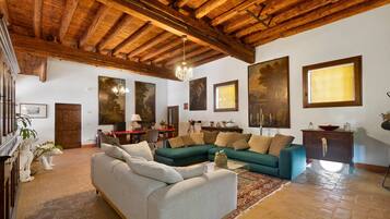 Uma sala de estar ampla com teto alto de madeira, um sofá verde, um sofá branco e um espaço de jantar com mesa e cadeiras.