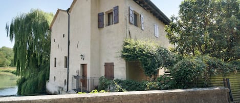 A two-story building with a sloped roof, wooden shutters, and a stone wall in front.