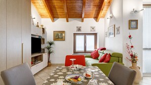 A dining area with a table set for two, a television, and a sofa in the background. - Holiday Home 'Dimora Chiaretta' with Balcony, Wi-Fi and Air Conditioning (Caronno Pertusella)