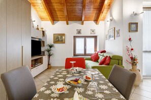 Ein Essbereich mit Tisch für zwei Personen, einem Fernseher und einer Couch im Hintergrund.