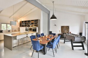 A modern kitchen with a dining area, a foosball table, and a large decorative wall piece.