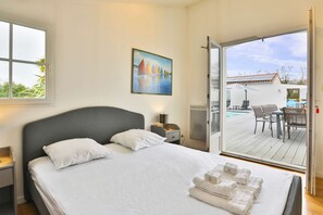 A bedroom with a bed, a nightstand, a painting, and a view of an outdoor deck with a table and chairs.