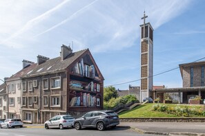 A multi-story building with a prominent tower, a street with parked cars, and a grassy area with flowers. - Comme Un Pacha - Nausicaá & plage à 700 m (Boulogne-Sur-Mer)