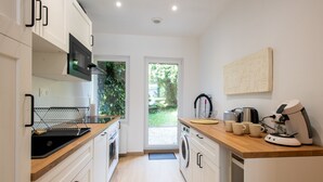 A modern kitchen with a microwave, oven, and washing machine. There is a wooden countertop and a coffee machine. - Comme Un Pacha - Nausicaá & plage à 700 m (Boulogne-Sur-Mer)