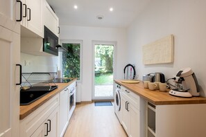 A modern kitchen with a microwave, oven, and washing machine. There is a wooden countertop and a coffee machine. - Comme Un Pacha - Nausicaá & plage à 700 m (Boulogne-Sur-Mer)