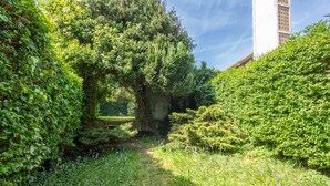 A lush garden with a pathway, dense foliage, and a building in the background. - Comme Un Pacha - Nausicaá & plage à 700 m (Boulogne-Sur-Mer)