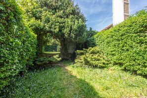 A lush garden with a pathway, dense foliage, and a building in the background. - Comme Un Pacha - Nausicaá & plage à 700 m (Boulogne-Sur-Mer)