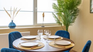 A dining table set for four with blue chairs, a vase with dried plants, and a large green plant in the background. - Comme Un Pacha - Nausicaá & plage à 700 m (Boulogne-Sur-Mer)