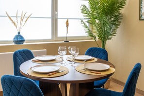 A dining table set for four with blue chairs, a vase with dried plants, and a large green plant in the background. - Comme Un Pacha - Nausicaá & plage à 700 m (Boulogne-Sur-Mer)