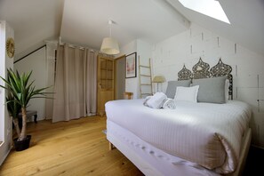 Ein Schlafzimmer mit einem Bett, einer Topfpflanze, Holzboden, einem Dachfenster und einer weißen Wand mit Dekorationselementen.