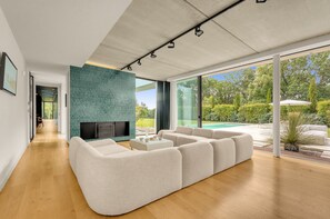 Un salon moderne doté d’un grand canapé d’angle, d’un téléviseur à écran plat et offrant une vue sur une piscine.
