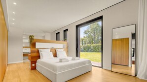 Ein modernes Schlafzimmer mit einem großen Bett, einem Holzkopfstück und Blick auf einen Garten.