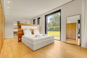 Une chambre moderne avec un grand lit, une tête de lit en bois et une vue sur un jardin.