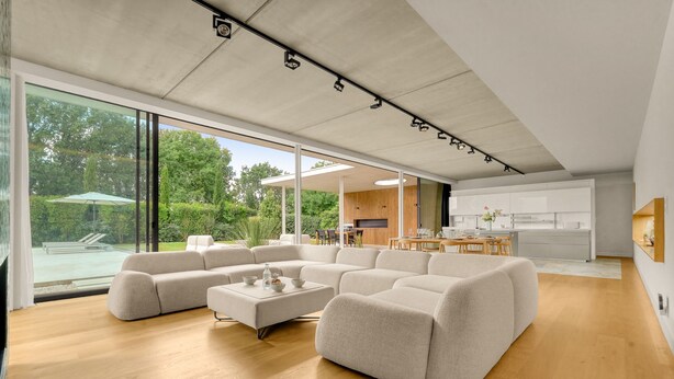 Ein großzügiger Wohnbereich mit einer großen Eckcouch, einem Couchtisch und Blick auf Pool und Garten durch große Fenster.
