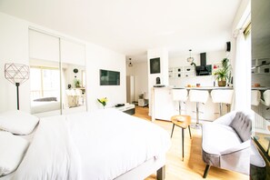 A modern hotel room with a large bed, a sitting area with a chair, a small table, and a kitchen area with a dining table. - Mouffetard Studio - À moins d'1 km du métro (Paris)
