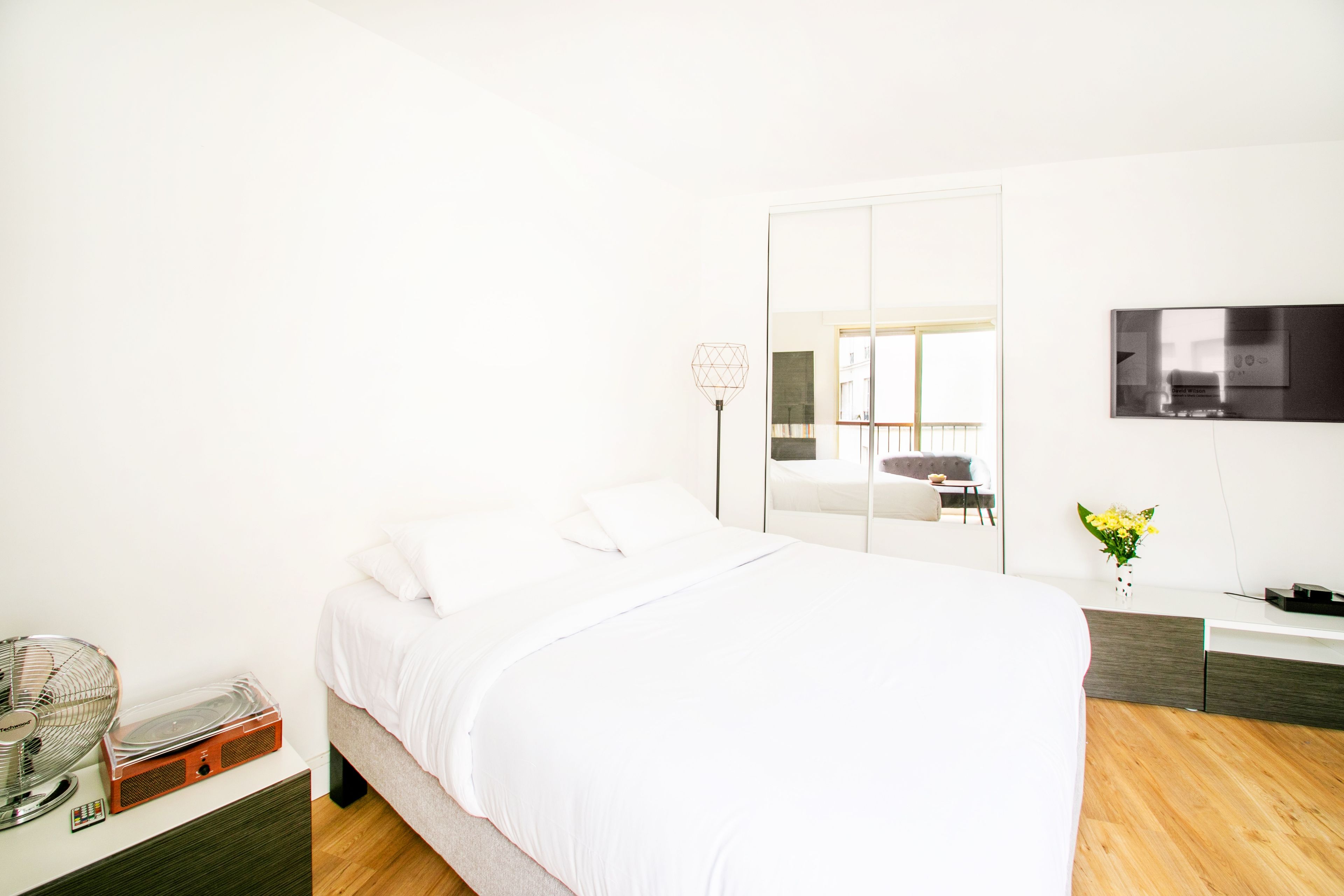 Een moderne slaapkamer met een bed, nachtkastje, spiegel en een televisie.