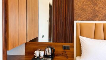 Habitación de hotel con una cama, un escritorio de madera con una bandeja de tazas y una tetera, un cubo de basura y un espejo grande.