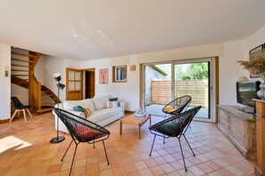 Ein Wohnzimmer mit einer Couch, zwei Sesseln, einem Couchtisch, einem Fernseher und einer Treppe.