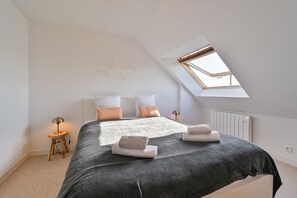 Ein Schlafzimmer mit Oberlicht, einem Bett mit Kissen, einem Nachttisch mit Lampe und einer Heizung.