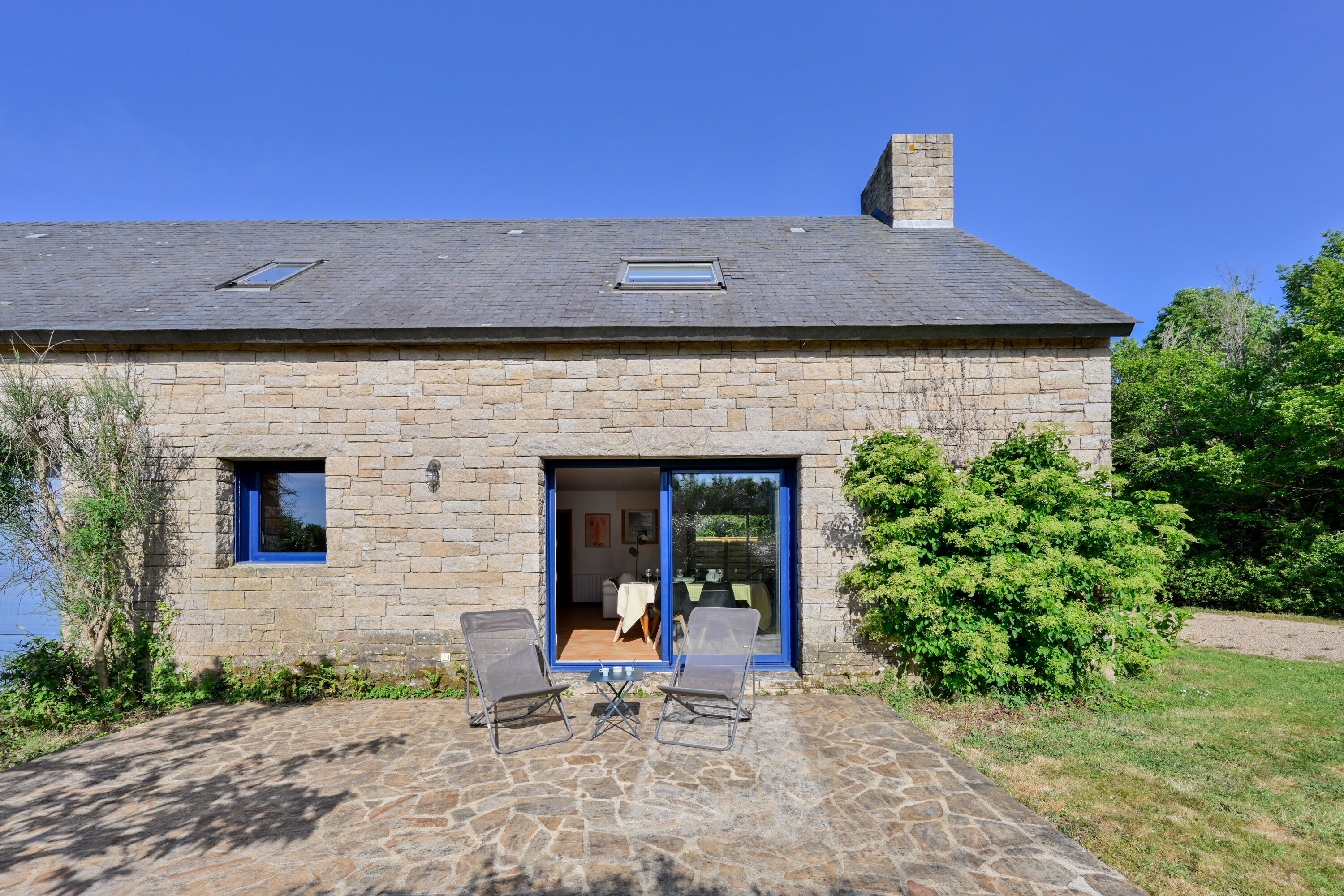 A stone house with a patio, two chairs, and a table.