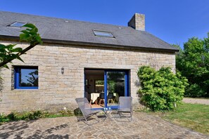 Ein Steinhaus mit Terrasse, zwei Stühlen und einem Tisch.