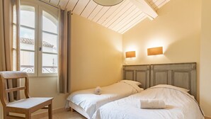 Una stanza con due letti, una sedia in legno, una finestra con tende e un soffitto con travi in legno.