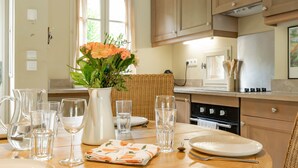 Una cucina con un tavolo da pranzo per due persone, una brocca, bicchieri e un vaso con fiori.