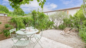 Una terrazza con un tavolo rotondo e sedie, immersa nel verde e con un edificio bianco dotato di tetto in tegole.