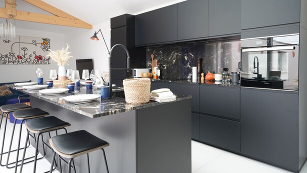 Een moderne keuken met donkere kastjes, een marmeren aanrechtblad, barkrukken en een groot schiereiland.