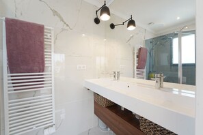 Ein modernes Badezimmer mit weißem Marmorfliesenspiegel, einem großen Spiegel, einer weißen Arbeitsplatte und einer Dusche mit Glastür.