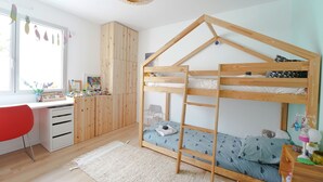 Een stapelbed met houten frame, een bureau met lades, een rode stoel en een raam met decoraties.