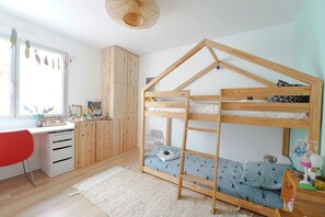 Ein Stockbett mit Holzrahmen, ein Schreibtisch mit Schubladen, ein roter Stuhl und ein Fenster mit Verzierungen.