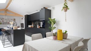 Een moderne keuken met donkere kastjes, een centraal eiland en een eethoek met een strepen tafelkleed.
