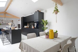 A modern kitchen with dark cabinetry, a central island, and a dining area with a striped tablecloth. - El Nido - charmante maison de vacances (Les Sables d'Olonne)