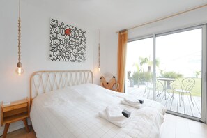 Ein Schlafzimmer mit Bett, Nachttisch, Wandbild und Blick ins Freie.