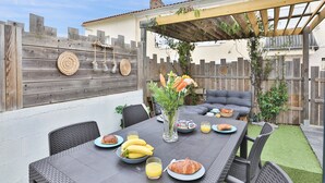 An outdoor patio with a table set for breakfast, including plates of food, a vase with flowers, and a wooden fence in the background. - L'Airial - Charmante maison aux Sables (Les Sables d'Olonne)