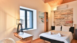 A bedroom with a bed, a desk, a window, a stone wall, and a bookshelf. - L'Airial - Charmante maison aux Sables (Les Sables d'Olonne)