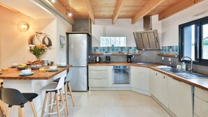 A modern kitchen with wooden beams, a built-in oven, and a large window. - L'Airial - Charmante maison aux Sables (Les Sables d'Olonne)