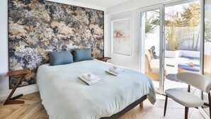 Ein Schlafzimmer mit einem großen Bett, Blick ins Freie und einem großflächigen Blumenbild an der Wand.