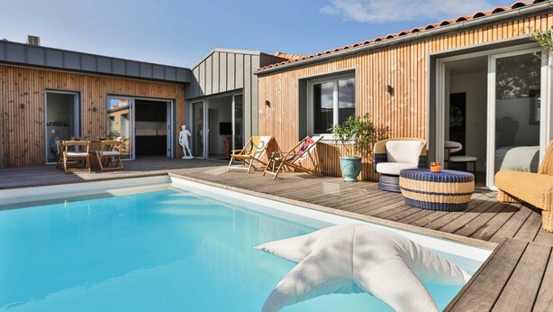 Ein modernes Haus mit Swimmingpool, Holzterrasse und Sitzgelegenheit im Freien.
